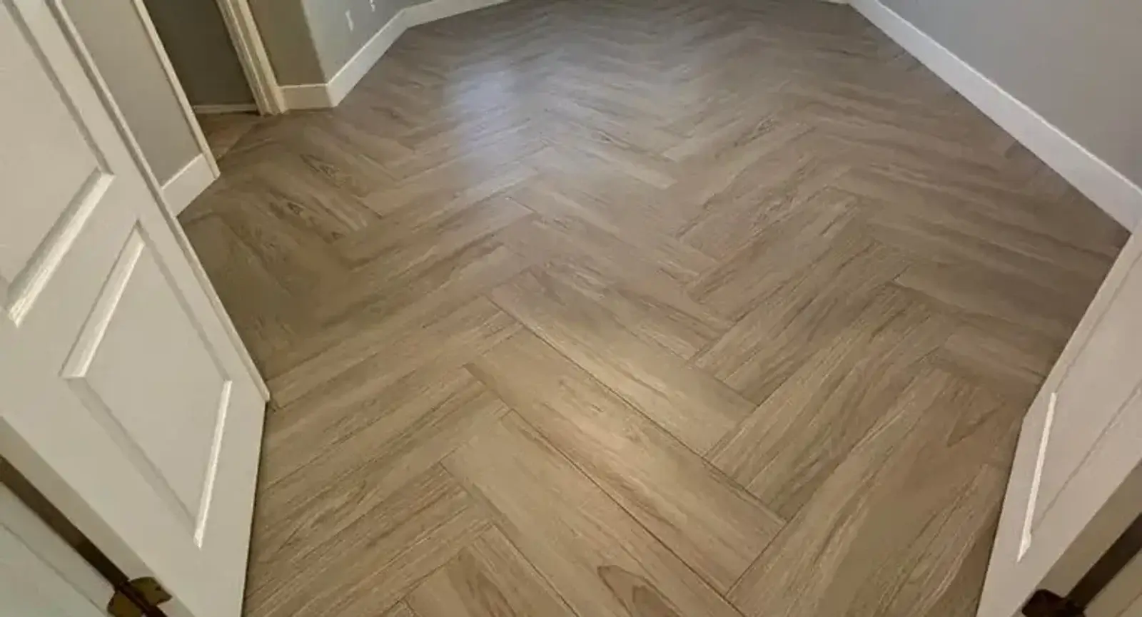 Light oak herringbone luxury vinyl plank flooring installed by Zona Floors in an Arizona bay-window sitting room, with a straight-plank LVP transition leading into the adjoining hallway