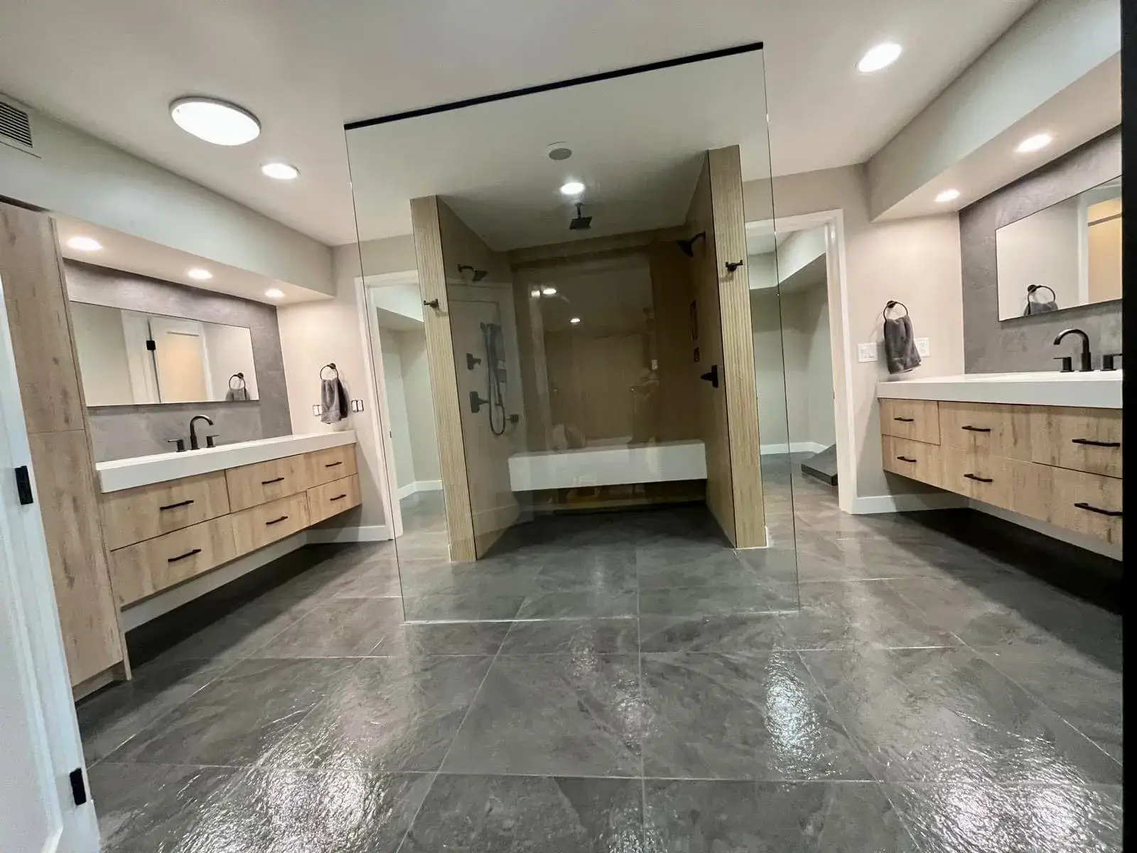 Modern Arizona master bathroom remodel by Zona Floors with floating wood vanities, walk-in glass shower, and large-format slate-look tile flooring