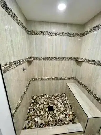 Custom walk-in shower with travertine walls, horizontal pebble-stone accent bands, and pebble shower floor by Zona Floors in Arizona