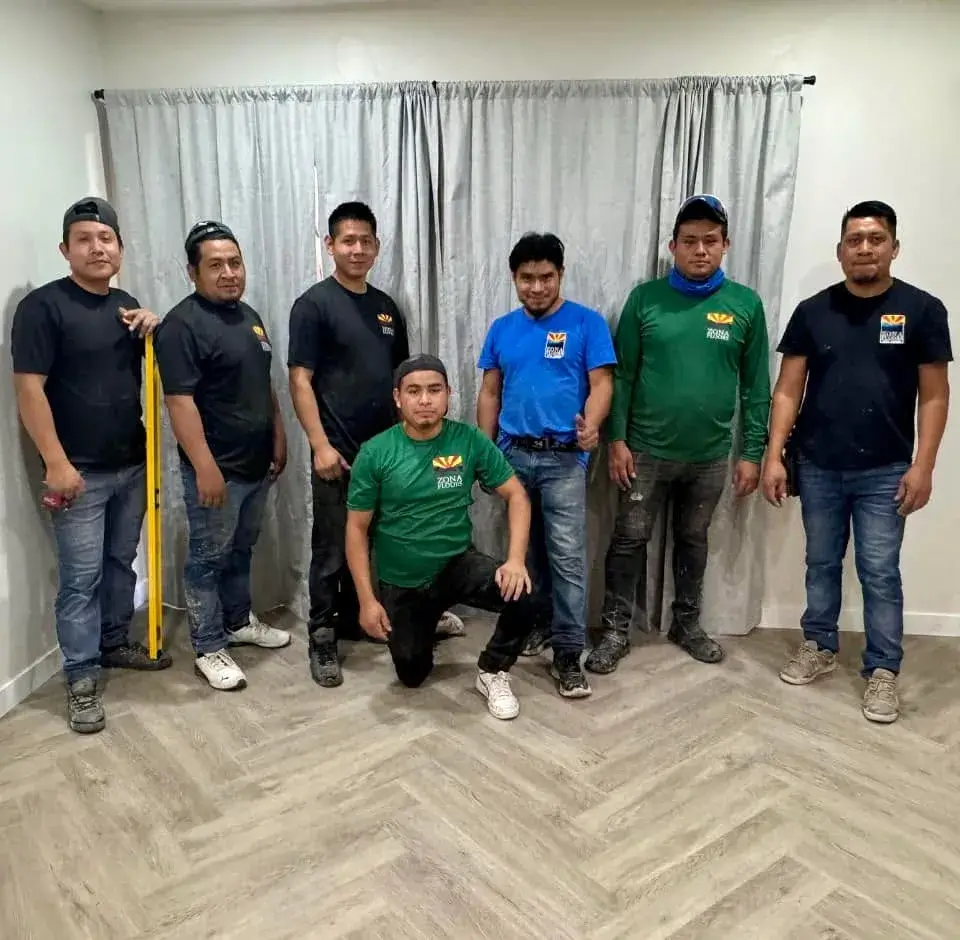 The full Zona Floors installation team in branded shirts standing on freshly-installed herringbone luxury vinyl plank flooring in an Arizona home