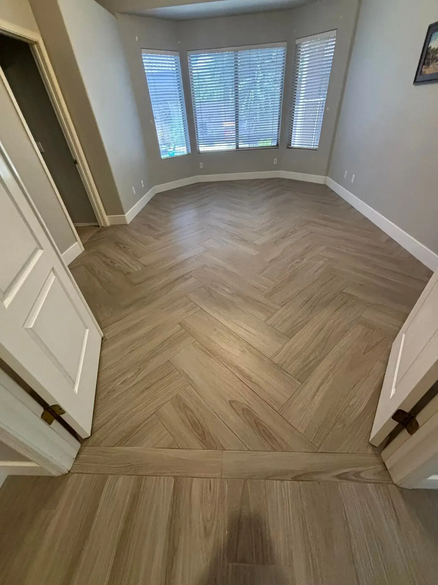 Light oak herringbone luxury vinyl plank flooring installed in an Arizona bay-window sitting nook by Zona Floors, transitioning to straight-plank LVP in the adjoining hallway