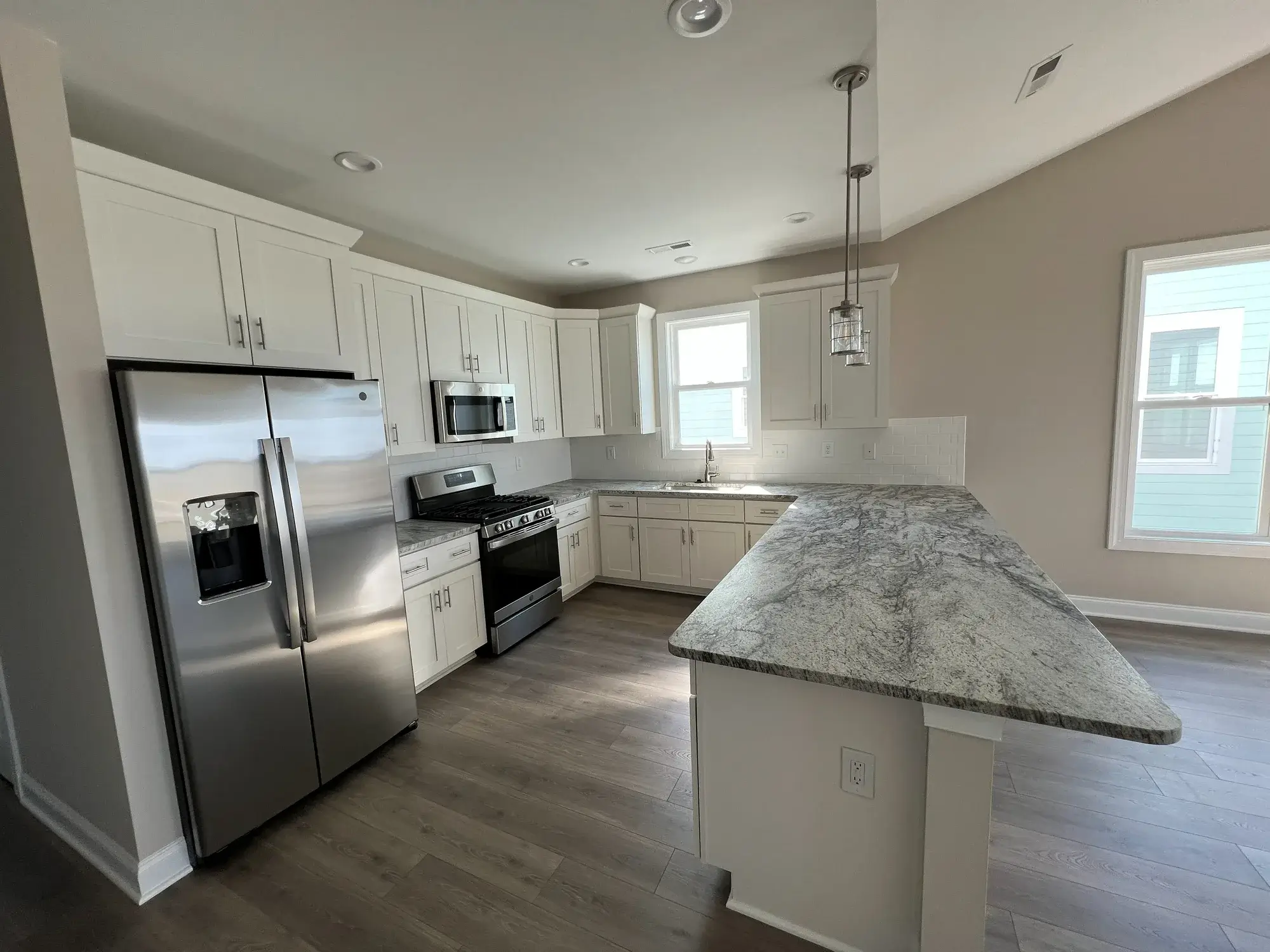 Completed open-plan kitchen remodel by Zona Floors in Arizona with white cabinets, granite island, stainless appliances, and engineered hardwood floors